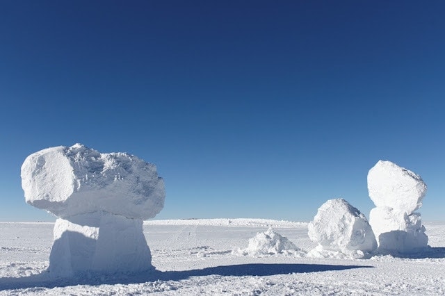 landscape in antarctica with three large ice stacks on a flat snowscape under bright blue sky. What its like working in Antarctica. 