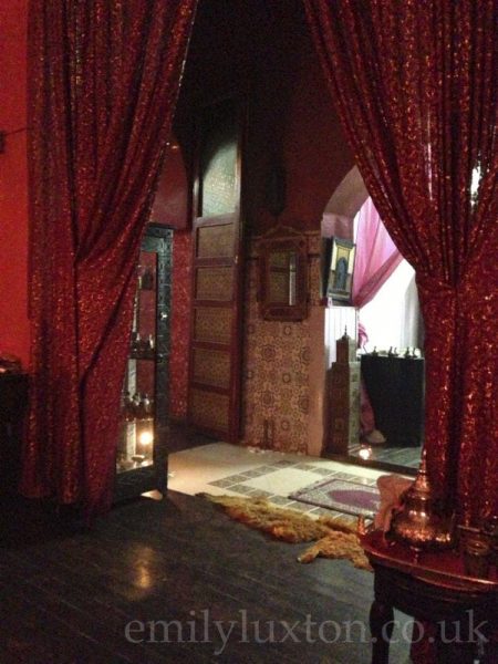 Interior of Hammam Ziani, a waiting room  with wooden floor, tiled walls, and red curtains with gold embroidery