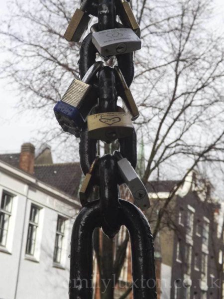 Close up of several padlocks hanging from a thick metal chain on the Love Lock bridge in Amsterdam