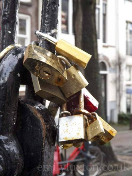 Close up of several padlocks hanging from a thick metal chain on the Love Lock bridge in Amsterdam