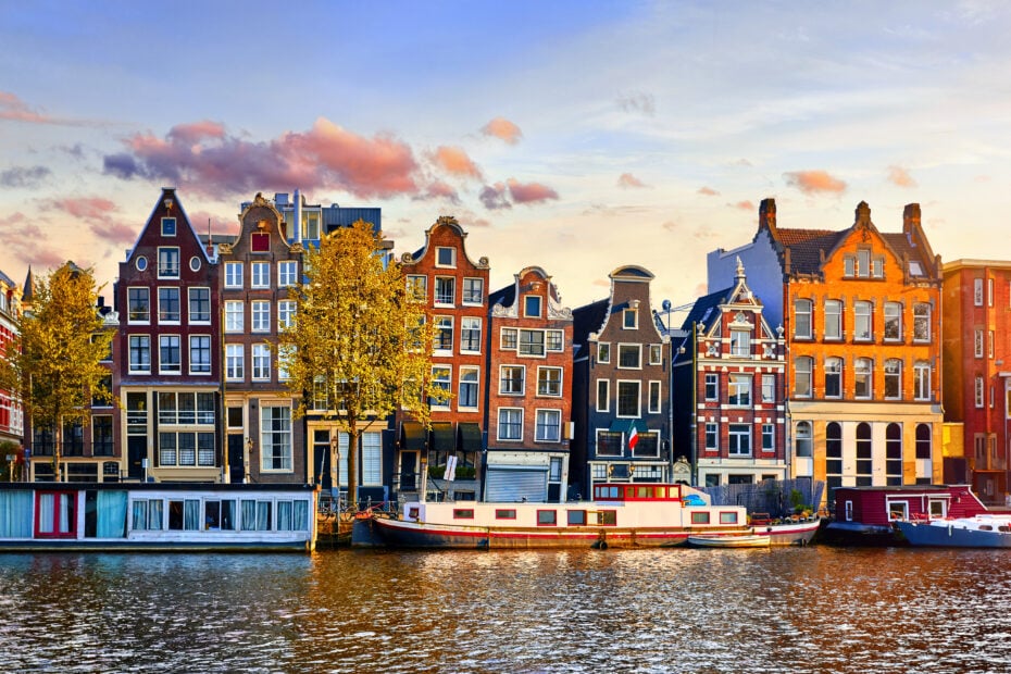 View of terraced townhouses across a river in Amsterdam Netherlands around sunset in spring with a canal boat on the watyer in front. One day in Amsterdam.