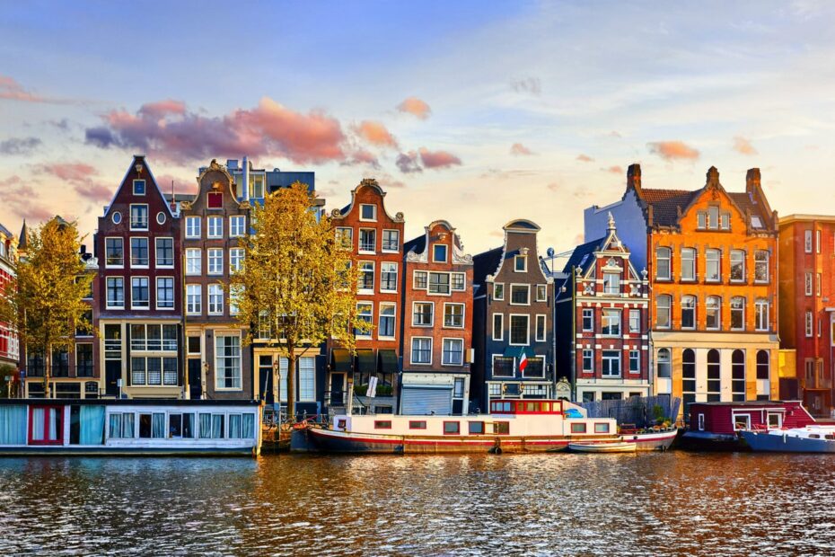 View of terraced townhouses across a river in Amsterdam Netherlands around sunset in spring with a canal boat on the watyer in front. One day in Amsterdam.