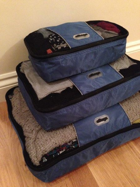 a stack of three blue ebags packing cubes in different sizes with the smallest on top stacked against a cream wall