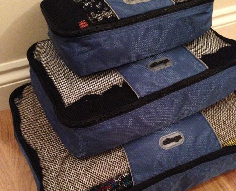 a stack of three blue ebags packing cubes in different sizes with the smallest on top stacked against a cream wall