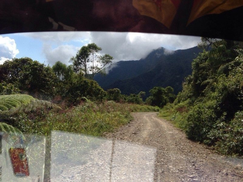 View of a gravel track through a bus window with mountains in the background