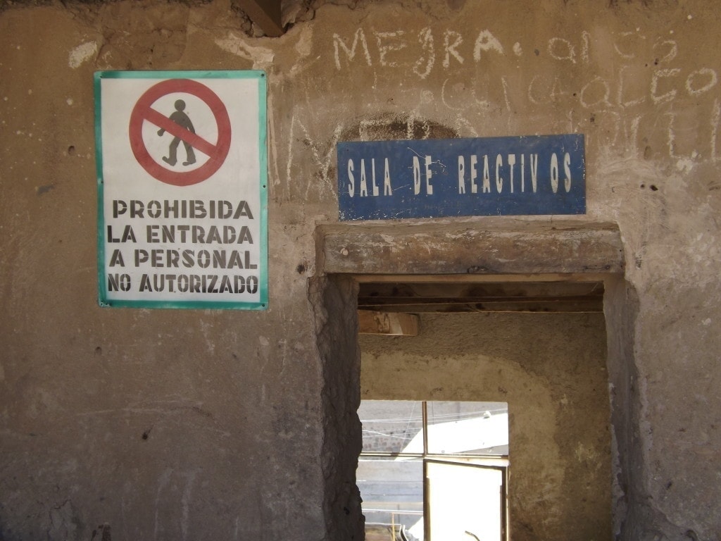 Doorway in a stone wall with two signs. A blue sign reads "Sala de Reactivos" and a white sign with a red no entry sign reads "prohibida la entrada a personal no autorizado"