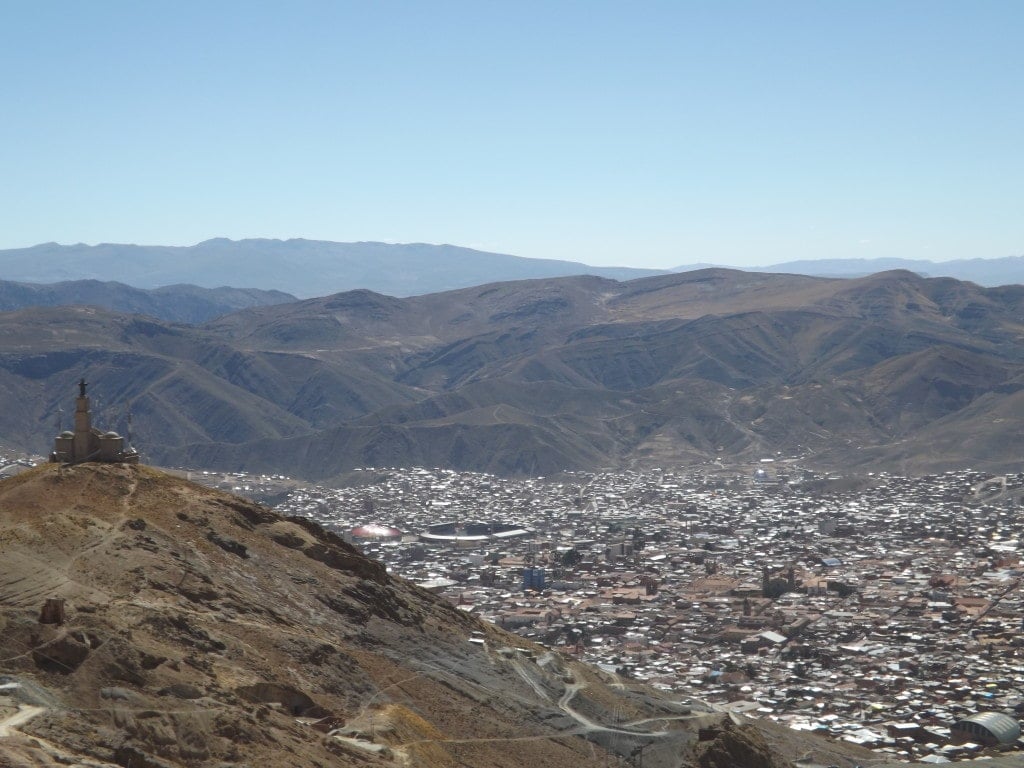 aerial shot of Potosi city skyline from a dusty brown rocky hillside with brown hills in the distance and clear blue sky above
