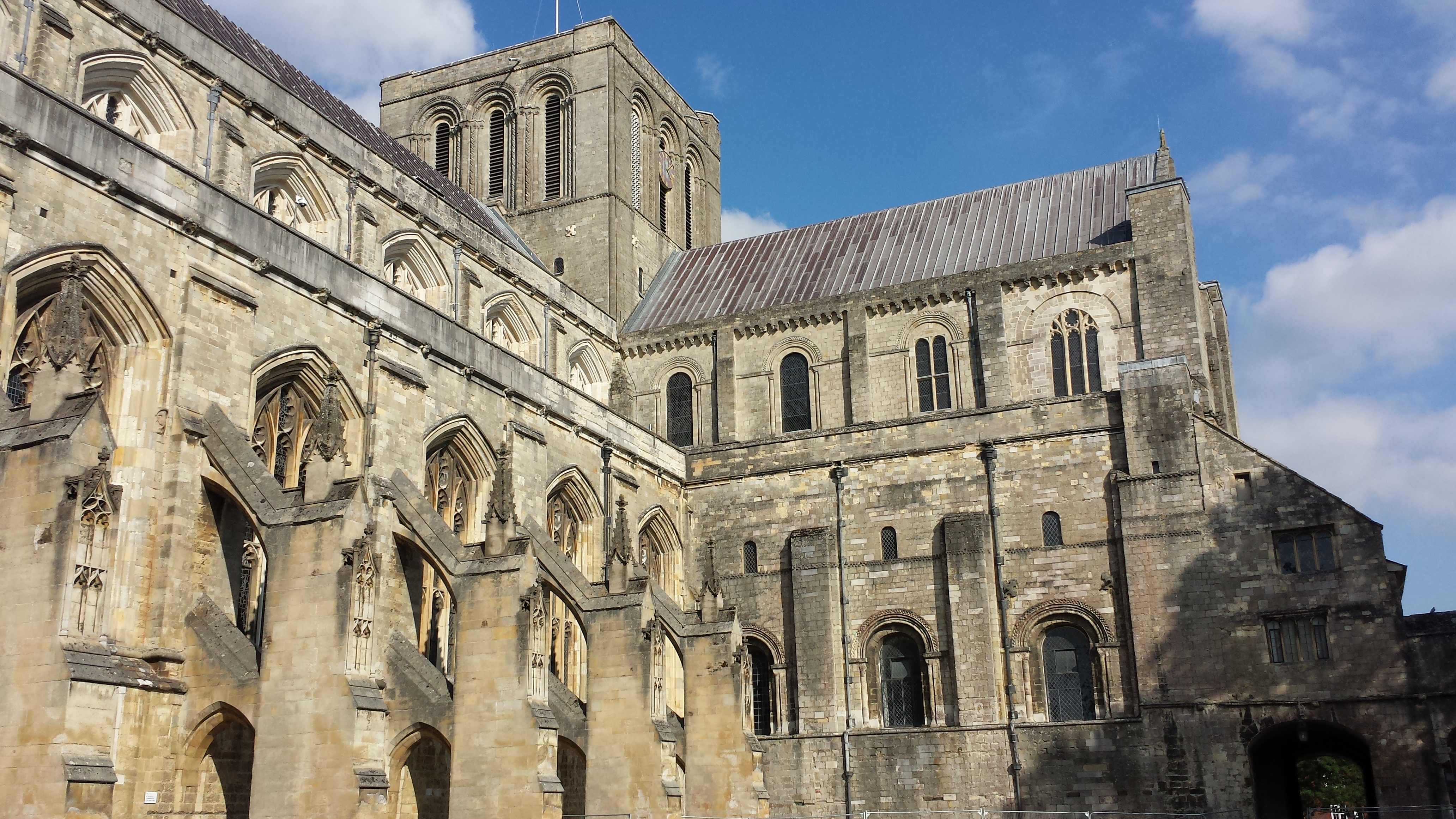 Exterior of Winchester Cathedral, a beige stone building with many different architectural styles and the square tower rising at its centre