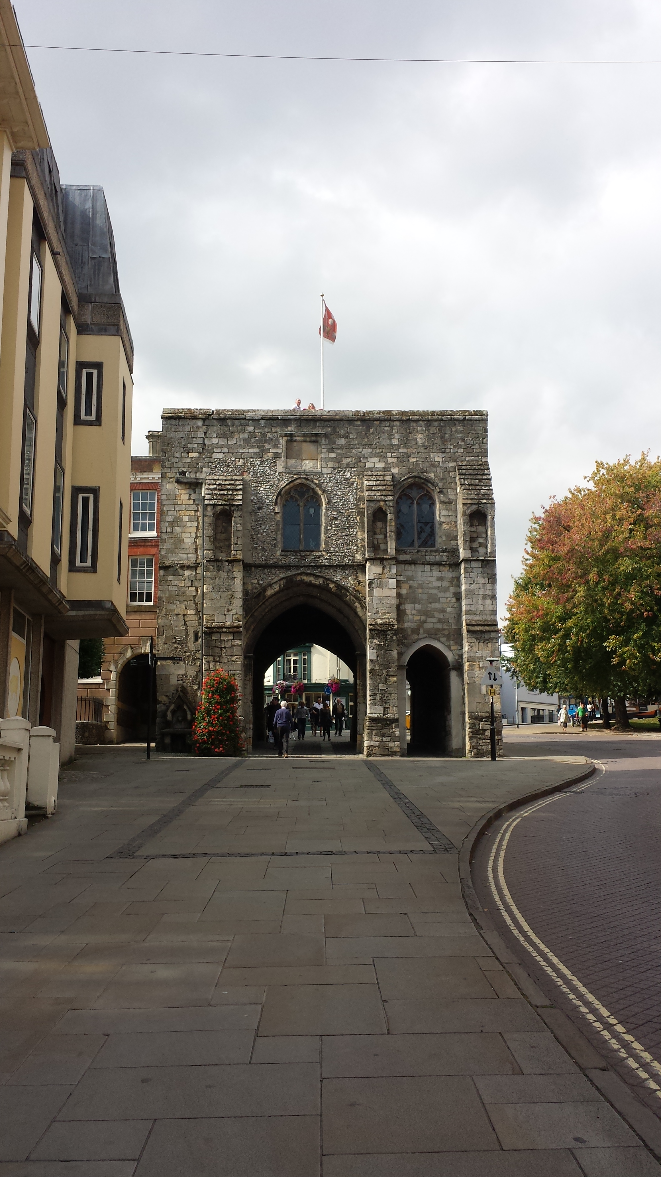 looking up the high street towards the medieval stone gatehouse known as Westgate in winchester, there is an archway at the base of the gatehouse where the gate used to be and a red flag on a flag pole at the top
