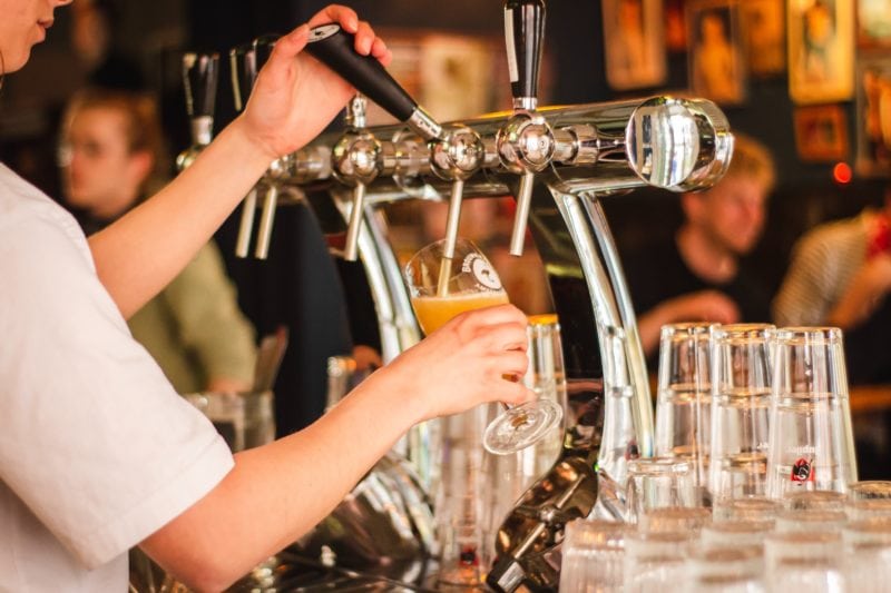 close up of a person's arm in a short sleeved white shirt holding a beer tap and pouring beer into a glass. Oktoberfest in the UK. 