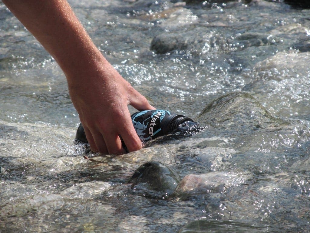Close up of a hand holding a black water bottle into a river to fill it up