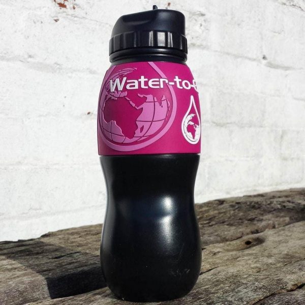 Close up of a black water bottle with a pink sleeve around it, standing on a wooden bench with a white wall behind. Water to Go Review
