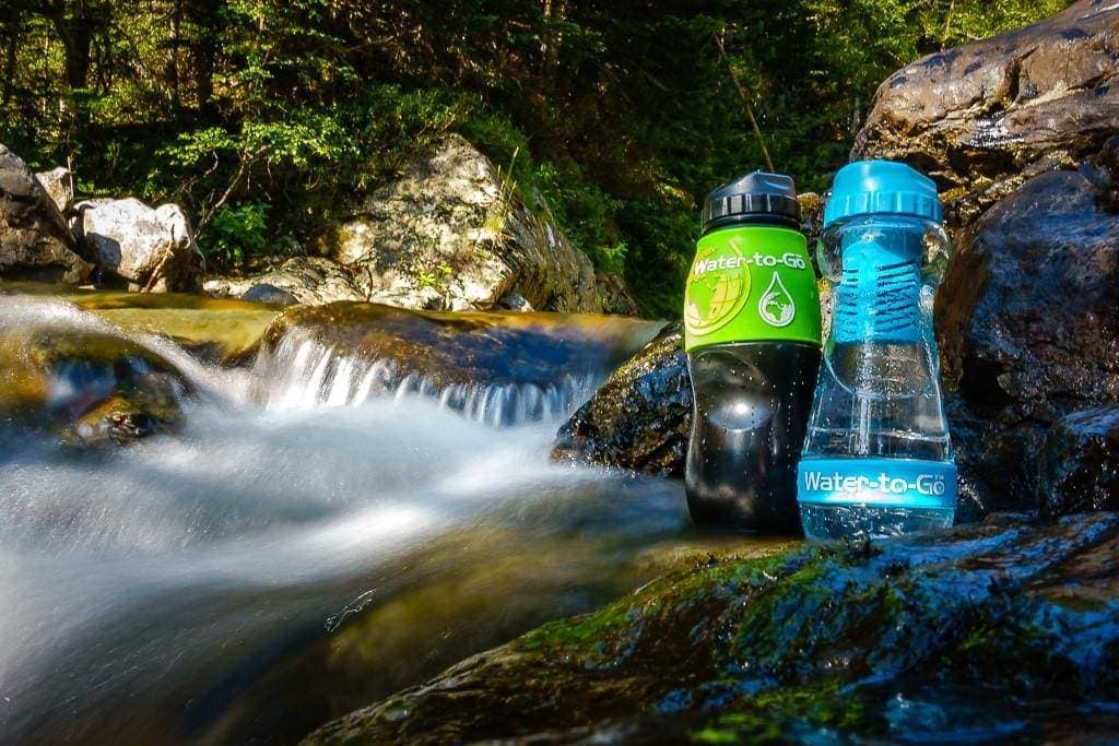 Two water bottles on a rocky ledge next to a mini waterfall in a stream surrounded by woodland. Water-to-Go review.