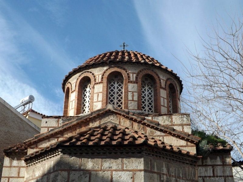 Top of an Ottoman church in Psirri district of Athens with grey walls and a circular top floor with red tiled roof against a clear blue sky