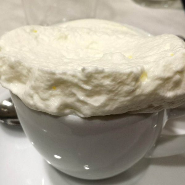 Close up of a small white mug topped with a large pile of whipped cream 