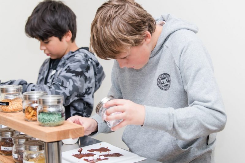 Two young boys wearing grey hoodies pouring chocolate into moulds at the Chocolatarium Edinburgh