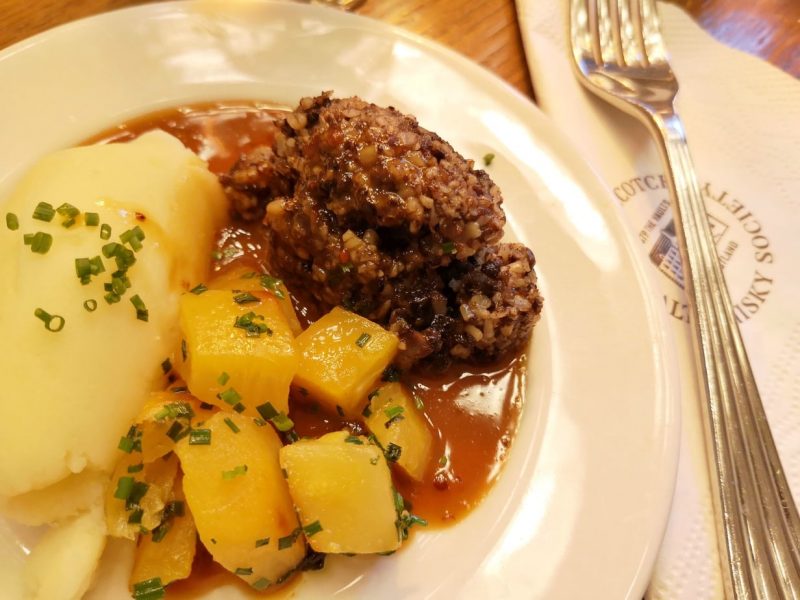 close up of a white plate with haggis, boiled sweed, mashed poatote, covered in gravy and chopped chives - taken on an Edinburgh food tour