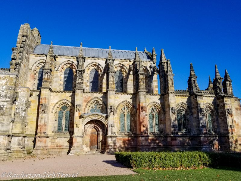 Rosslyn Chapel in Scotland, a historic stone church with many small tiers topped with stone triangles, taken on a sunny day with clear blue sky above