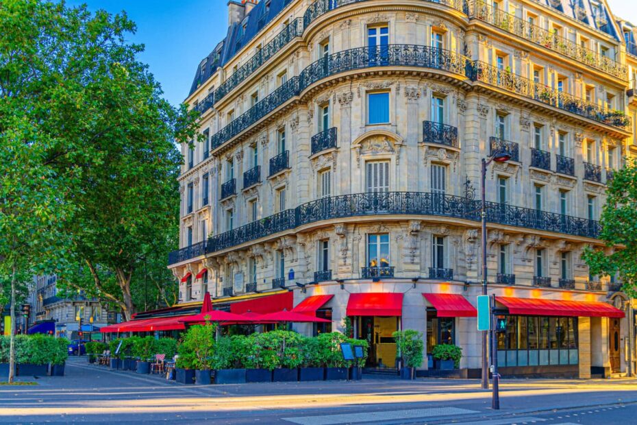 Tall cream coloured townhouse in Paris with a restaurant on the ground floor with red awning