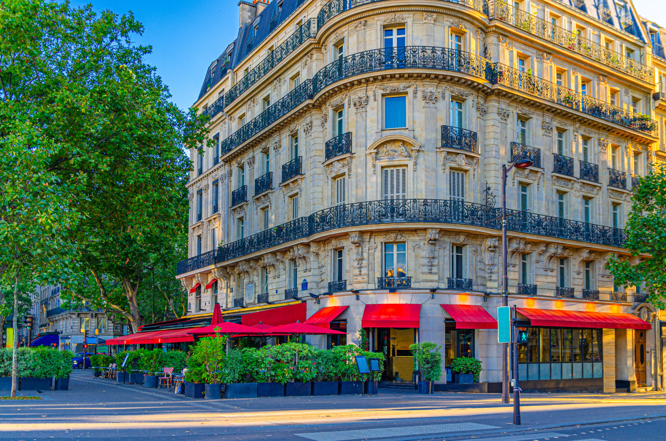 Tall cream coloured townhouse in Paris with a restaurant on the ground floor with red awning