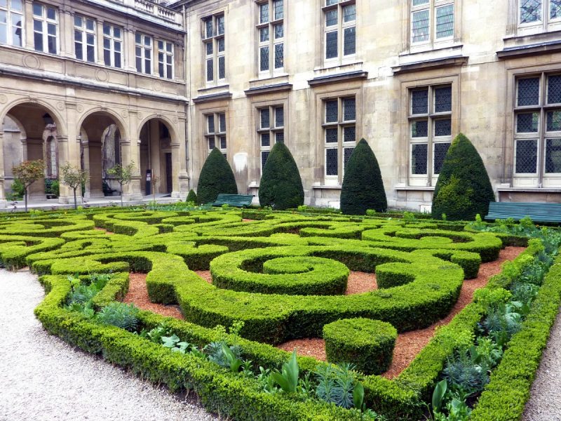 courtyard of a large historic mansion built from beige coloured stone with a miniature maze in the centre of the courtyard made of very low green hedges grown in a swirl design. unusual things to do in paris