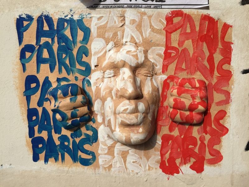 street art mural of a sculpted face with the word Paris painted over it in the colours of the french flag.