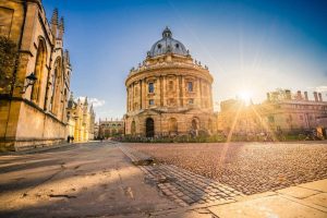 The Radcliffe Camera in Oxford, England, under a clear blue sky, surrounded by cobblestone streets and historic buildings.