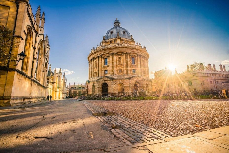 The Radcliffe Camera in Oxford, England, under a clear blue sky, surrounded by cobblestone streets and historic buildings.