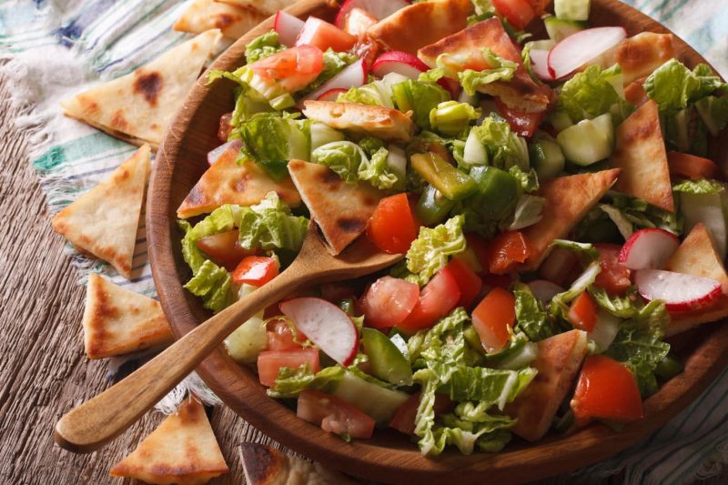 Close up of a fattoush salad with lettuce, cucumber, raddish and triangles of flatbread in a wooden bowl - dubai food guide