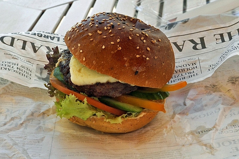 Close up of a camel burger in a bun with halloumi on a sheet of newspaper