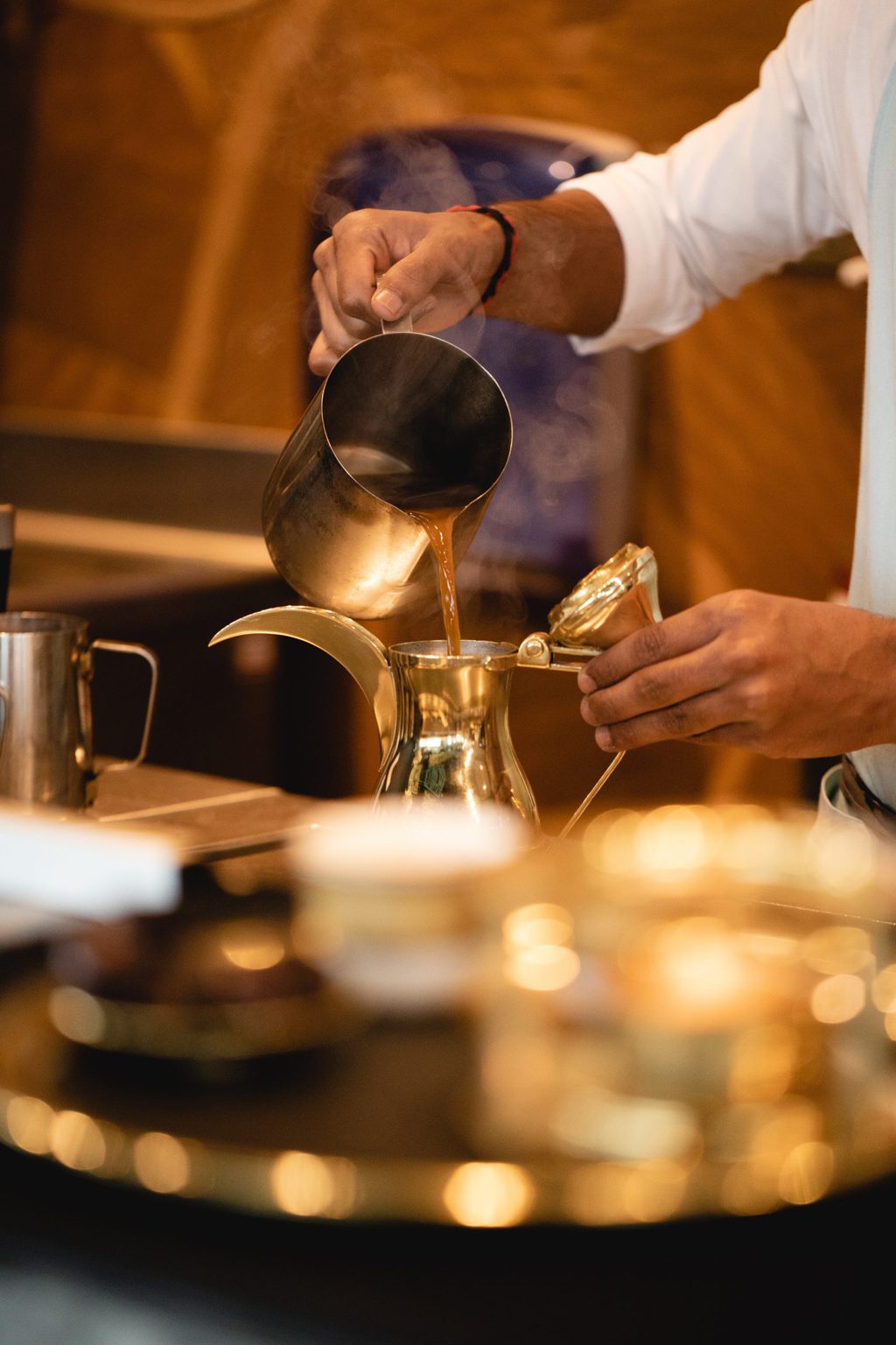 close up of coffee being poured from a silver jug into a curved silver coffee pot/