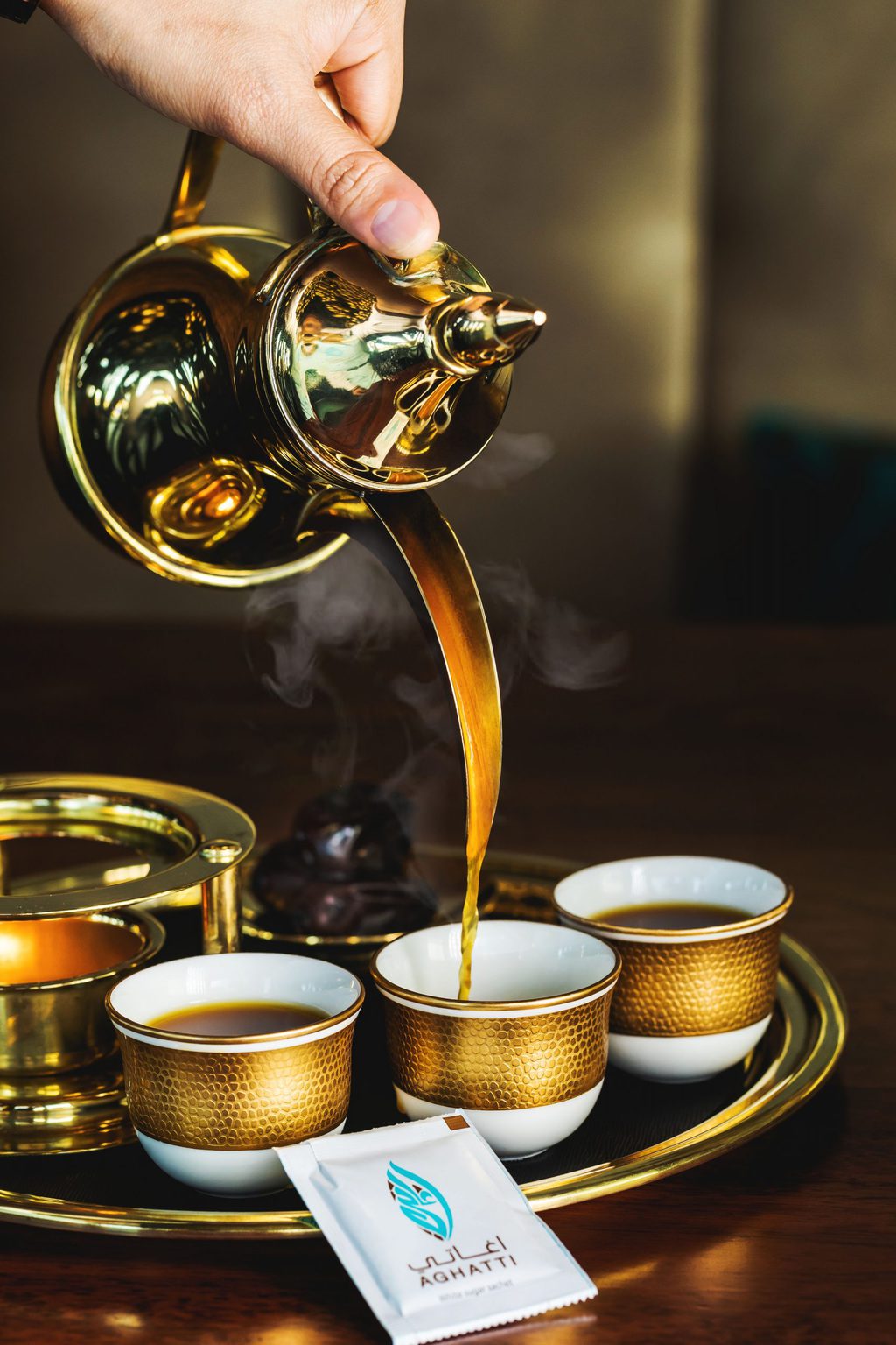 Arabic Coffee being poured from a gold coffee jug into small white china cups with gold edges, all on a gold tray, at a coffee shop in Dubai