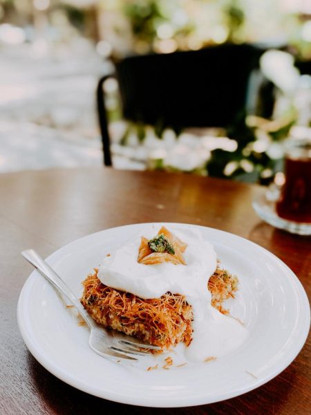 Kanafeh on a white china plate with the background out of focus. the kanefah looks like crispy brown noodles topped with a white cream. 