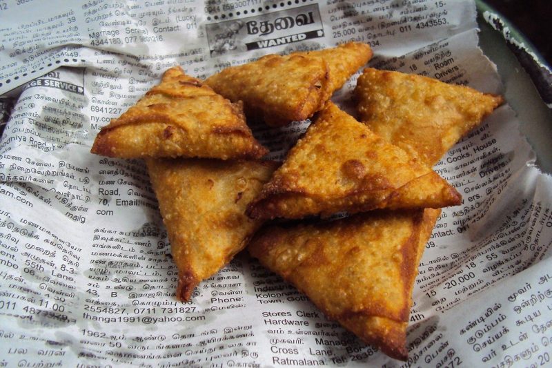 close up of some fried samosas on a sheet of newspaper with arabic writing