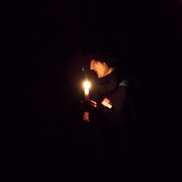 Very dark photo taken inside the Edinburgh Vaults with a lady's face and hand lit by the candle she is holding - but nothing else visible