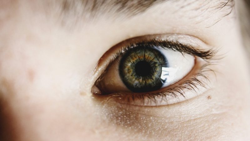 Close up of a human eye with green iris on a caucasion person's face with a freckle below the eye. Surviving Long Haul Flights.