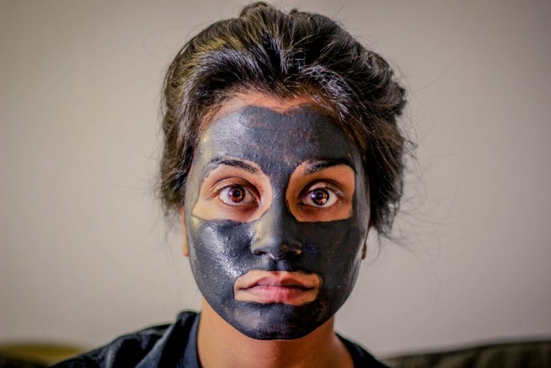 close up of a woman's face with a dark grey face mask on and her dark hair tied back. her eyes are brown and open wide and her mouth is expressionless. 