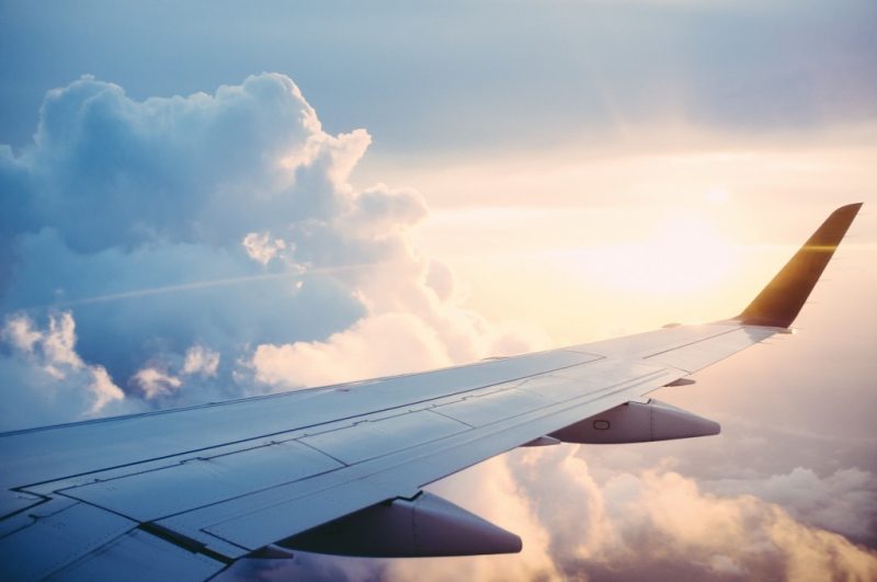 view from the plane window of an aeroplane wing in the sky with clouds all around and the sun blurred behind. Tips for long haul flights. 