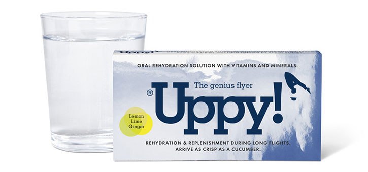 Blue box of Uppy rehydration tablets next to a glass of water on a white background. What to take on a long haul flight