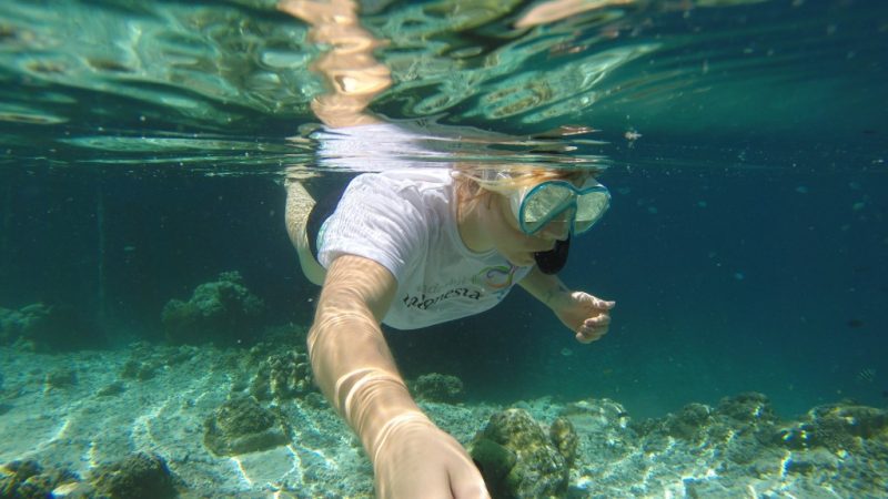 Underwater selfie of Emily wearing a snorkel and swimming in shallow clear water in Raja Ampat Indonesia