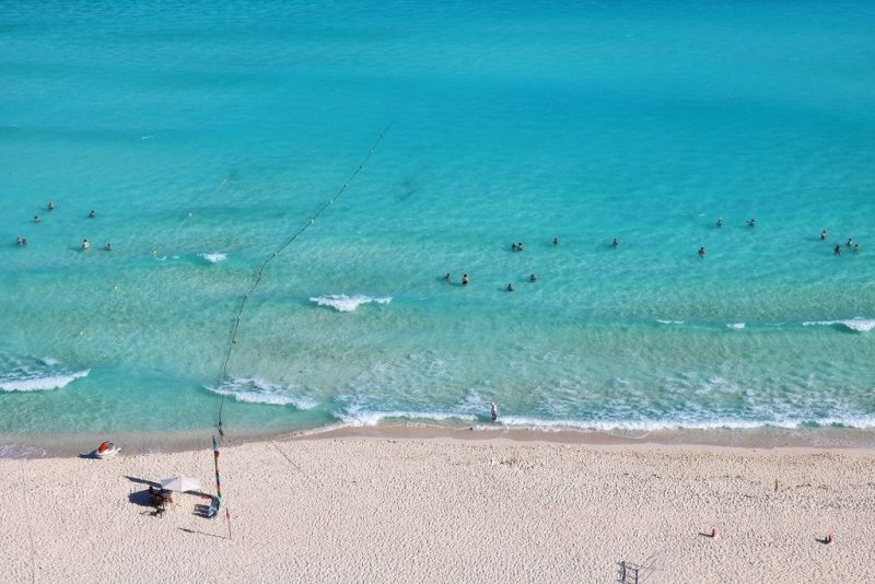 Aerial shot of a beach in Cancun with white sand and turquoise water and many people swinning in the sea. Is there Uber in Cancun.