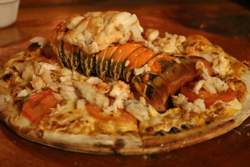 close up of a pizza topped with melted cheese and a large lobster tail in roots pizzeria holbox