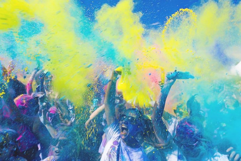 Crowd of men and woman throwing bright yellow and turquoise paint into the air at Holi in India