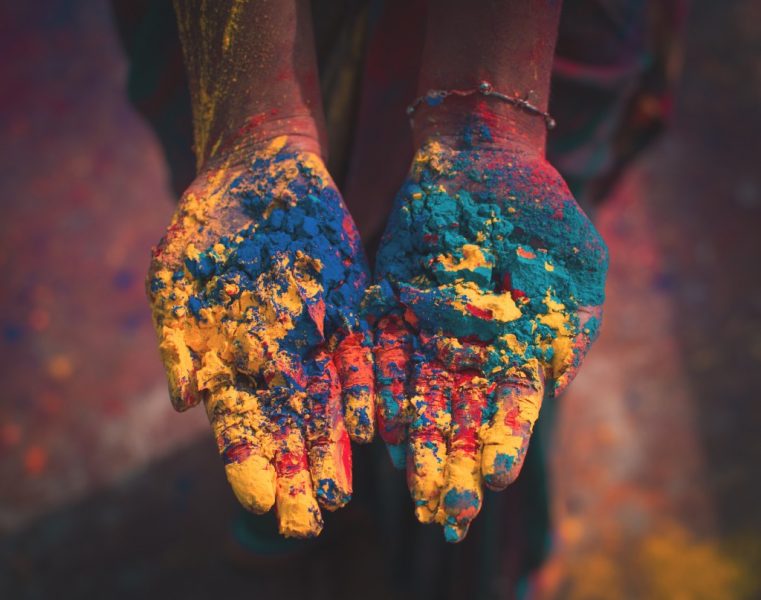 Close up of an Indian woman's hands palms-up covered in red, green, yellow and blue powder