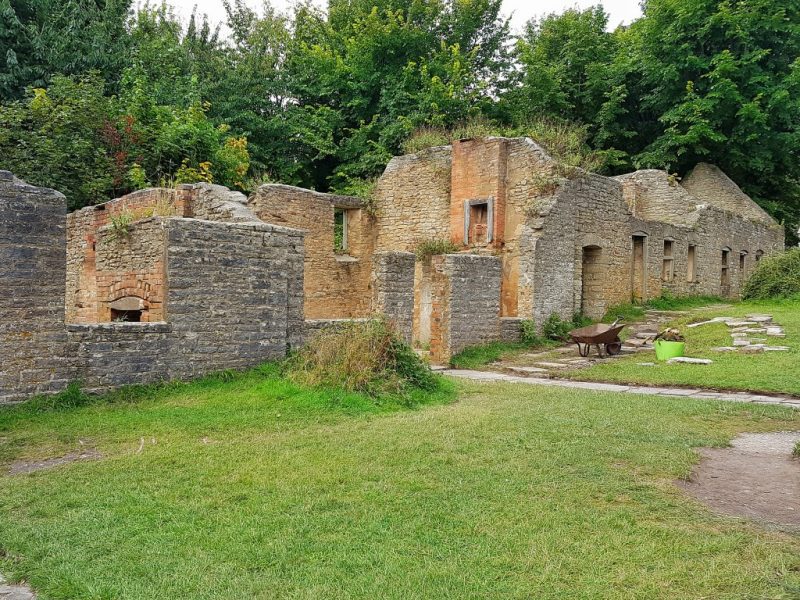 Ruined stone houses with empty windows and no roofs next to a grassy lawn with trees behind. 50 unique places dorset