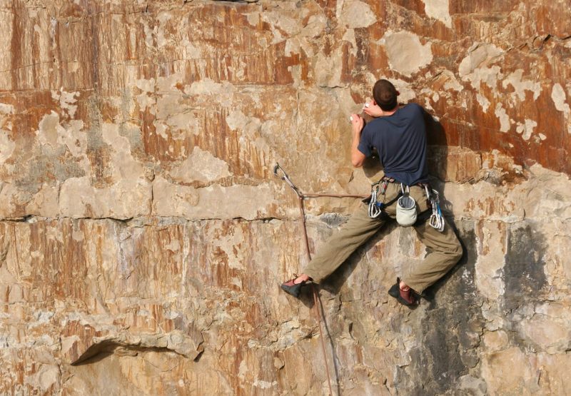 Man climbing on the side of a sheer orange coloured rocky cliff face on Portland in dorset