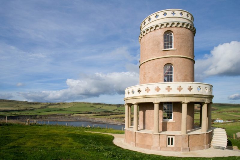 Four storey circular tower with smooth peach coloured walls and pillars around the bottom floor standing in a grassy field with countryside behind. Unique places to stay dorset