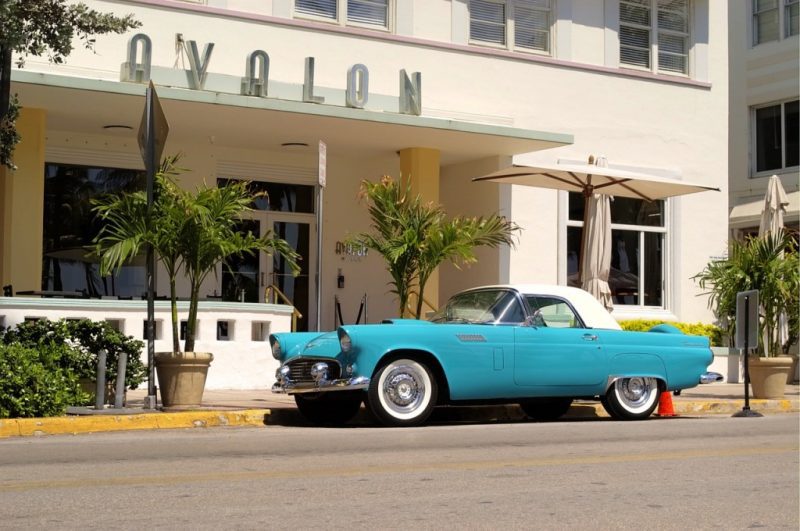 a blue classic car with a white roof outside a white art deco building with the sign Avalon. best miami food experiences.
