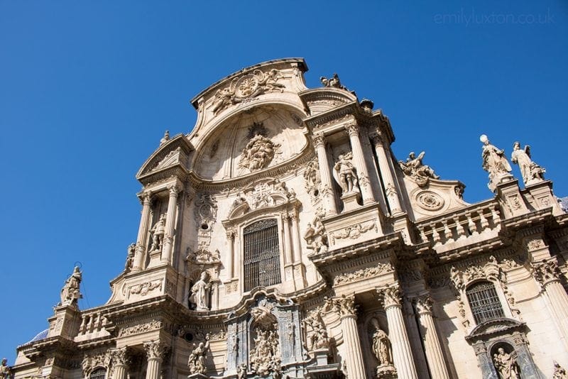 Looking up at the front of a church built from a cream coloured stone with an elaborately carved facade