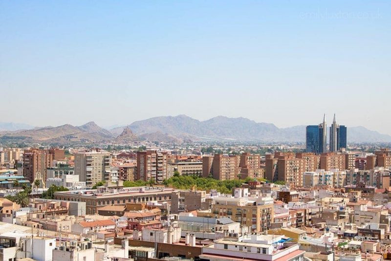 Murcia city skyline viewed from high - a city with many orange and pink coloured buildings and tower blocks with low mountains behind and blue sky above